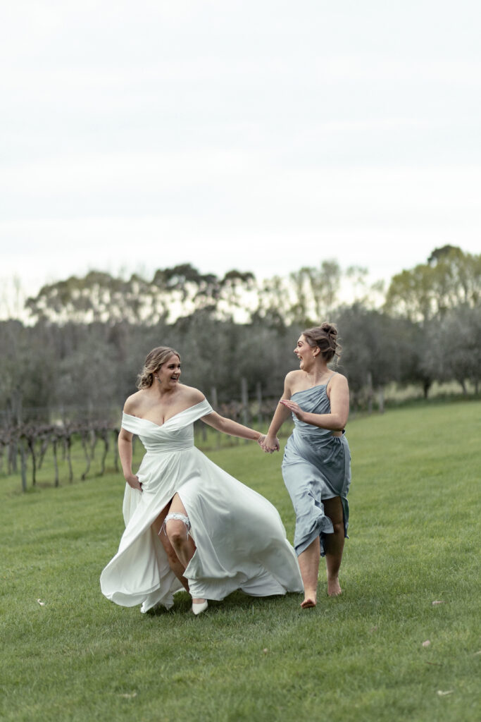 Bride running with her bridesmaid at Cossars Wineshed in Christchurch captured by Lavender Turner Photography.