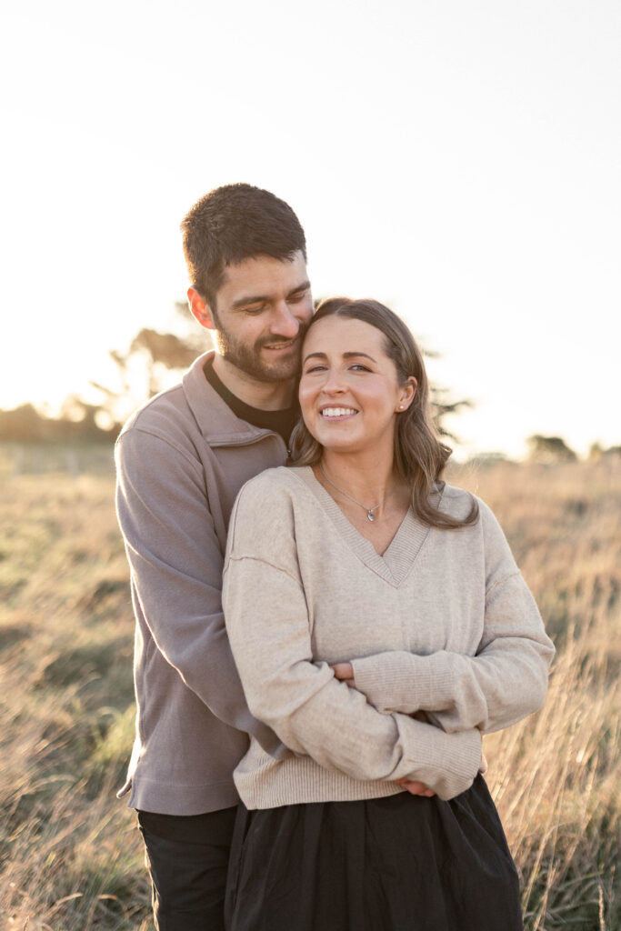 An engaged couple hugging in a golden-hour field in Christchurch, showcasing warm, natural light engagement photography.