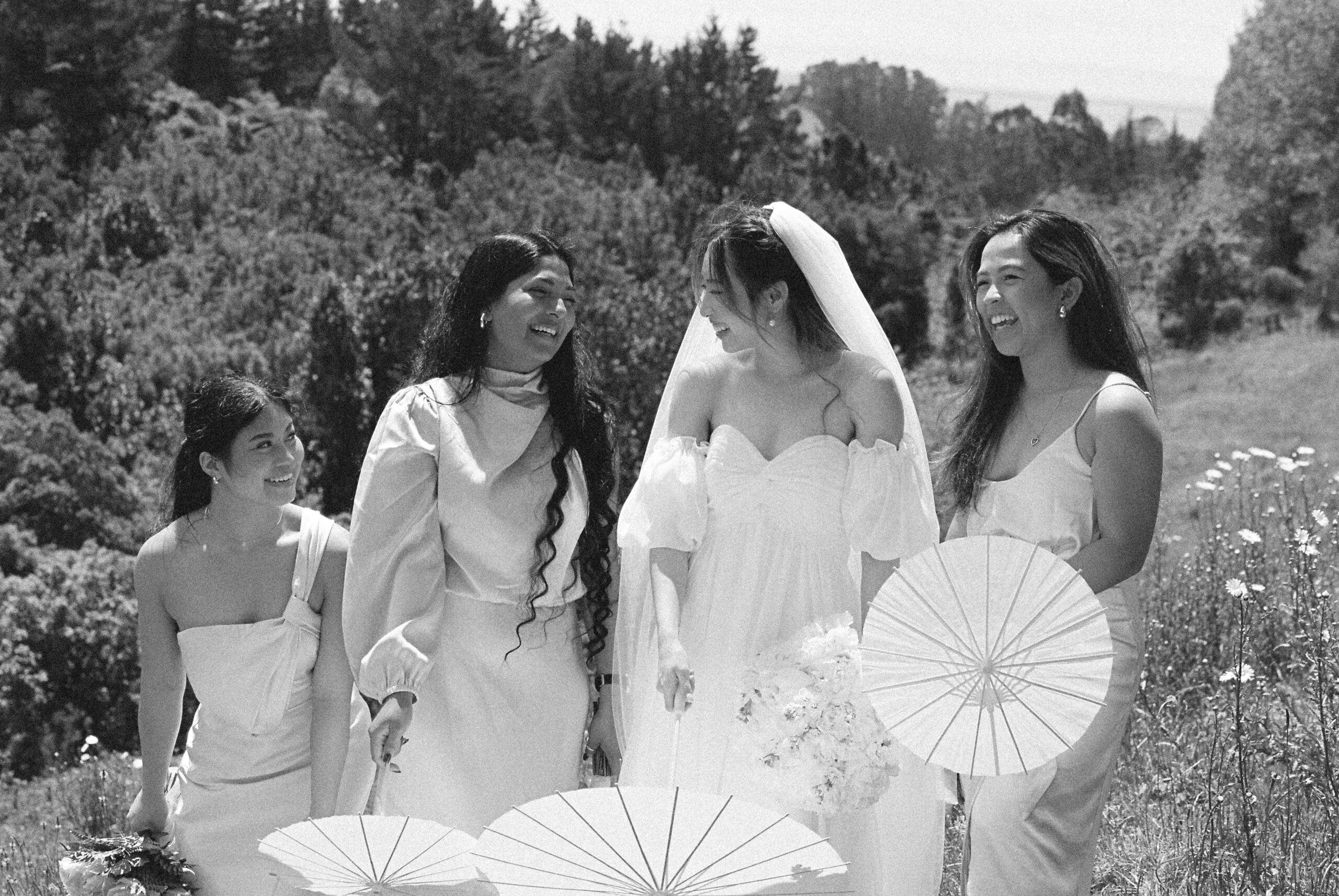The bride laughing with her bridesmaids outdoors, captured in black and white with soft light and natural expressions.
