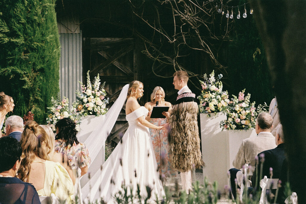 A bride and groom exchanging vows during an outdoor wedding ceremony, captured on film with soft light, natural colours, and a romantic garden setting.