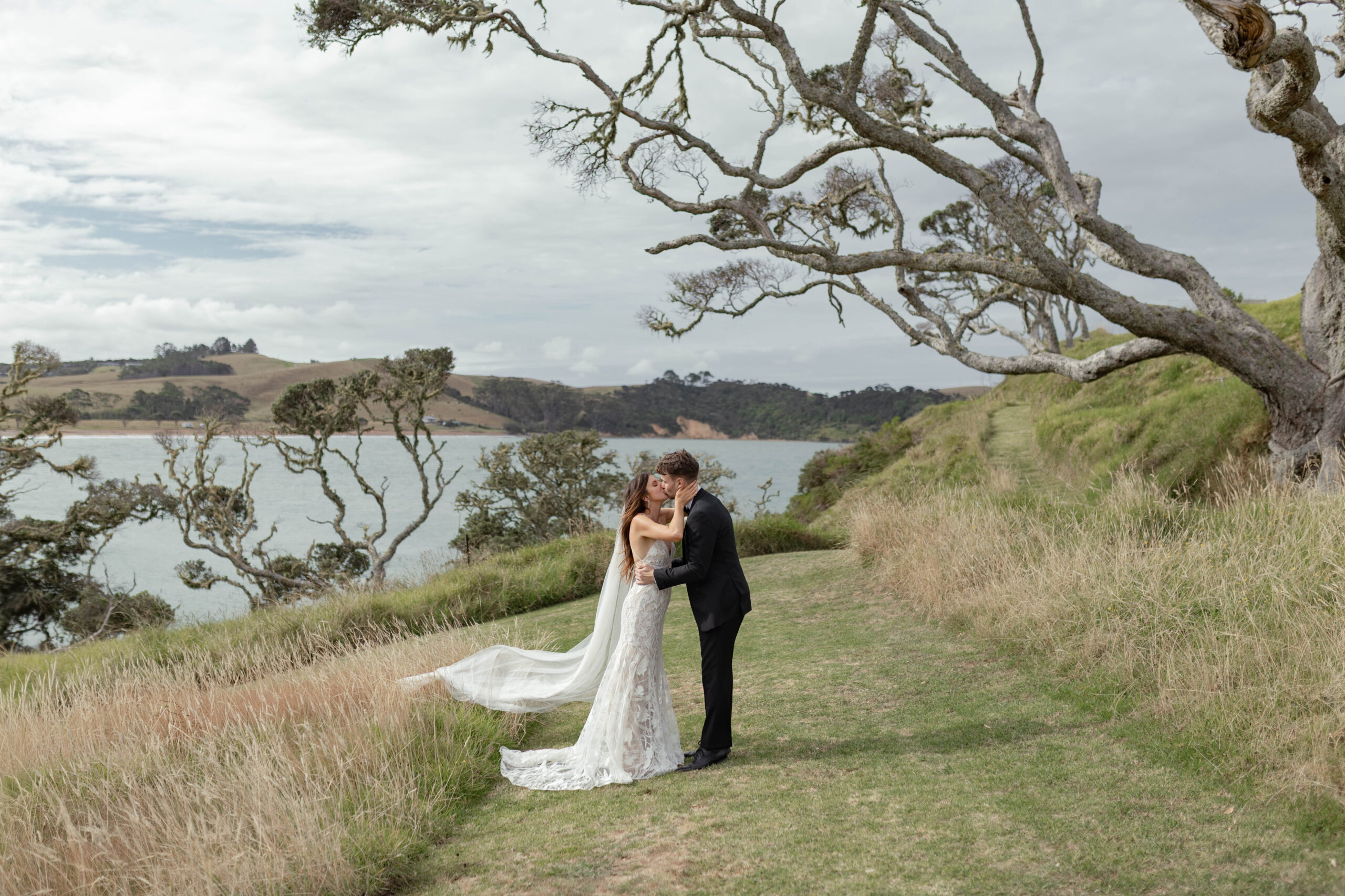 Bride and groom kissing at Baylys’ Farm wedding venue with coastal Bay of Islands views
