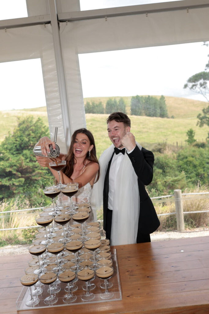 Bride and groom pouring espresso martinis into a champagne tower at Baylys’ Farm wedding reception