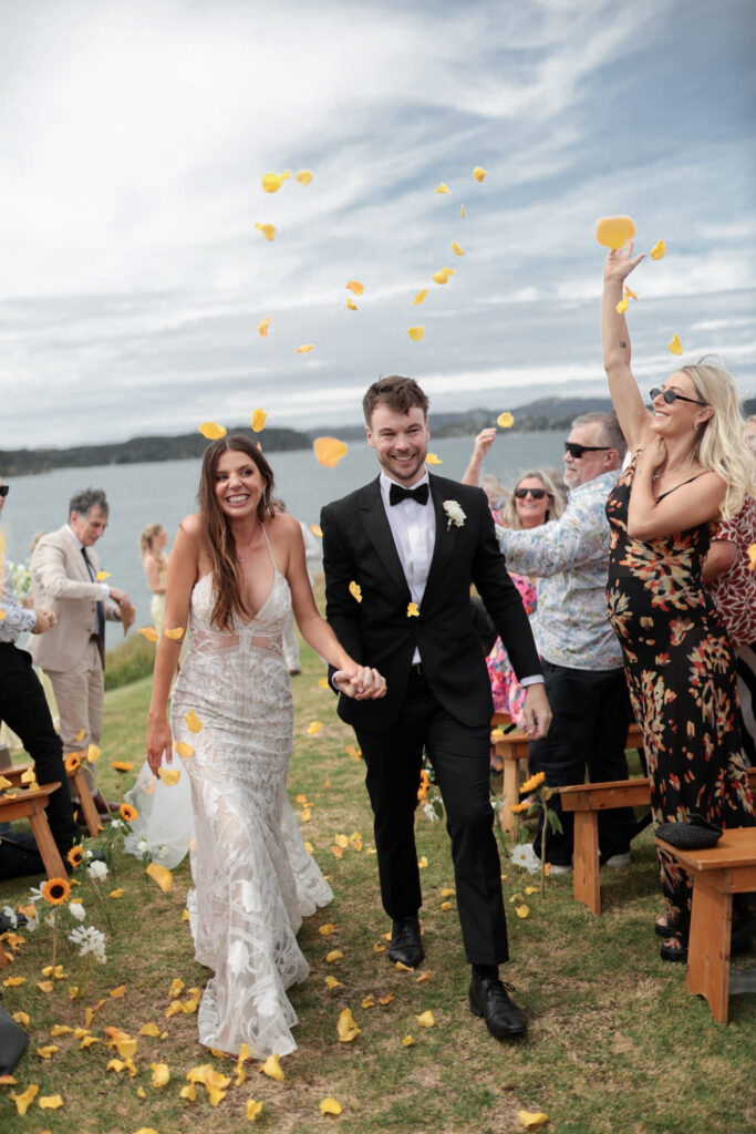 Bride and groom walking back down the aisle at Baylys’ Farm wedding venue in the Bay of Islands with yellow petal confetti